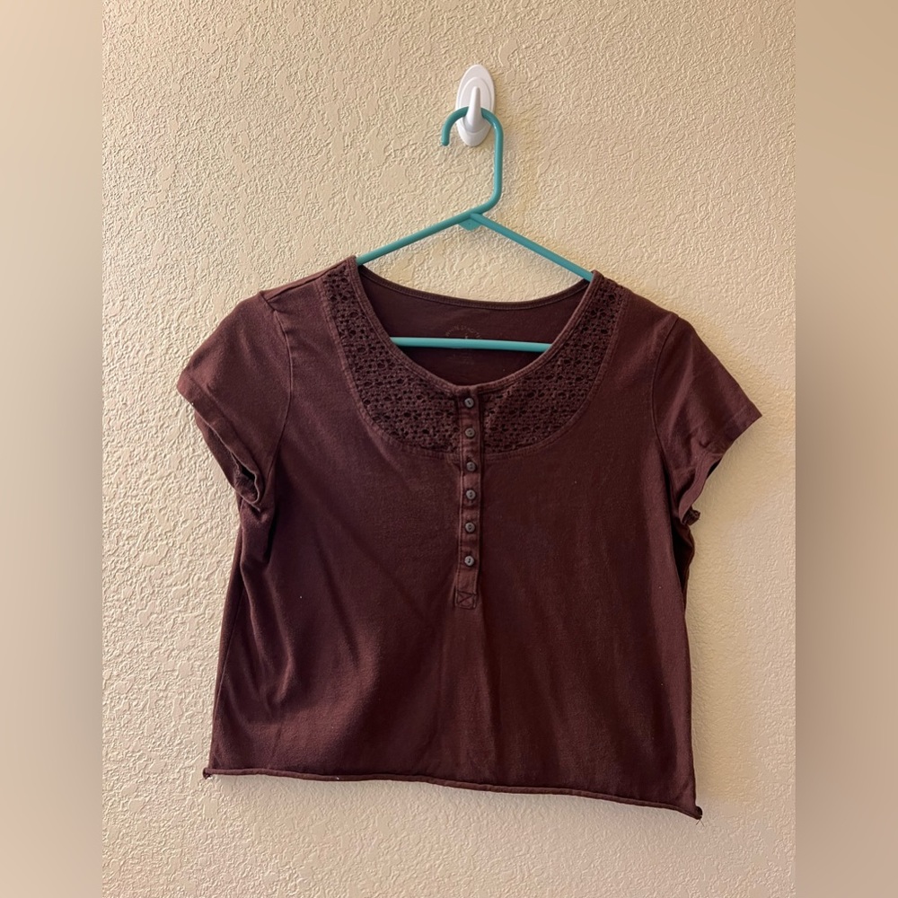 Brown shirt with brown buttons down the center. Crochet detailing at the top.
